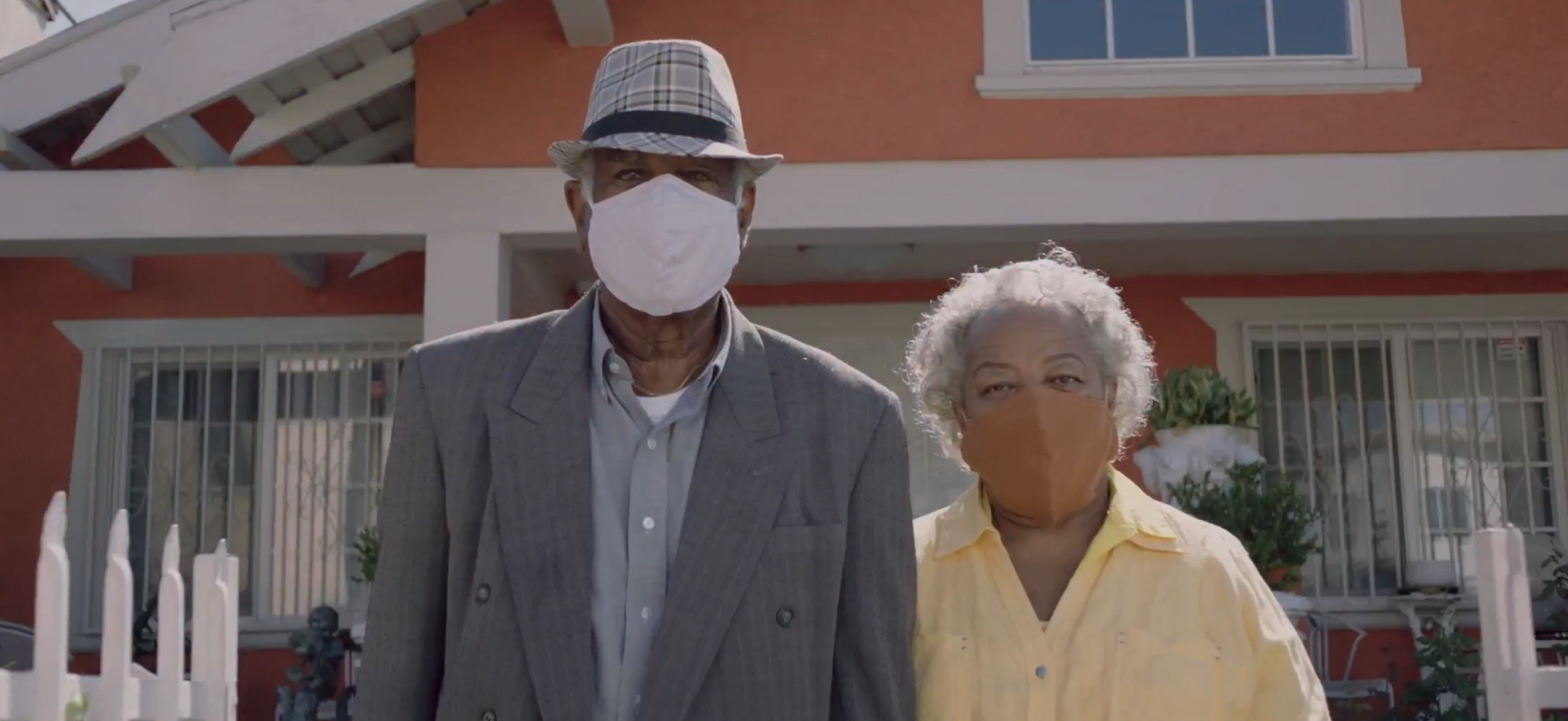 Casal de velhos usando máscaras em pé na frente de casa