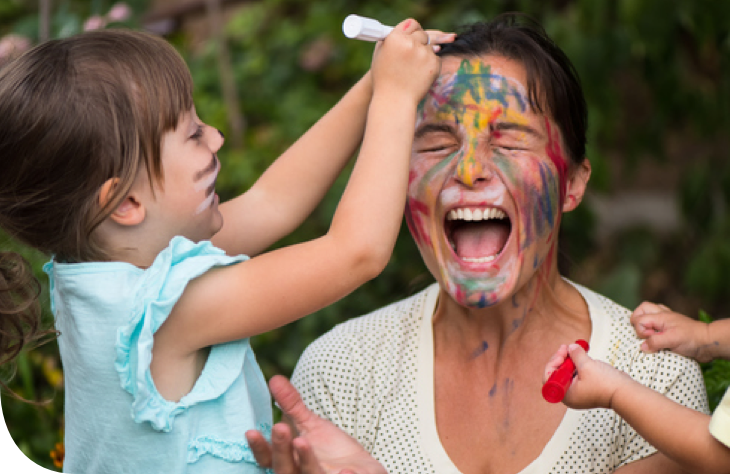 Criança desenhando no rosto de uma mulher com marcadores coloridos